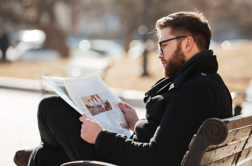 man reading newspaper on a park bench showing why weekend news consumption feels different